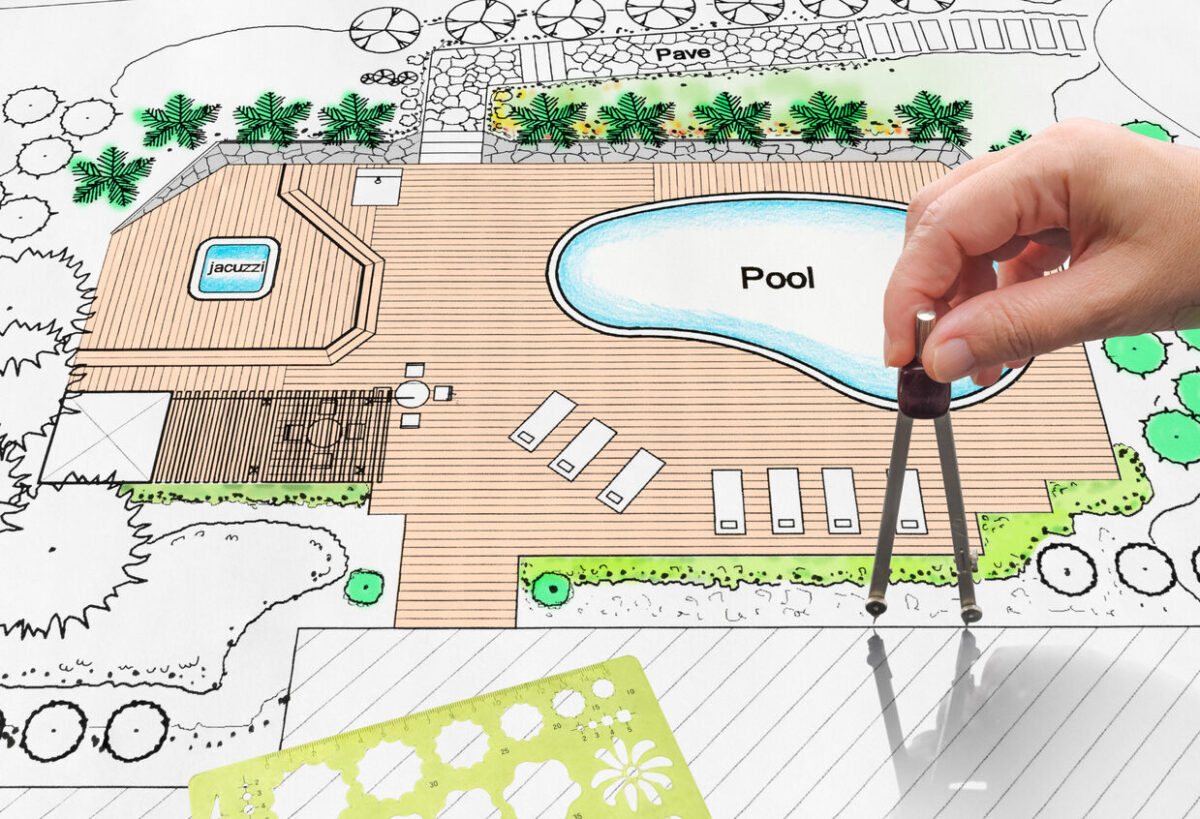 hand holding compass on house plan with pool
